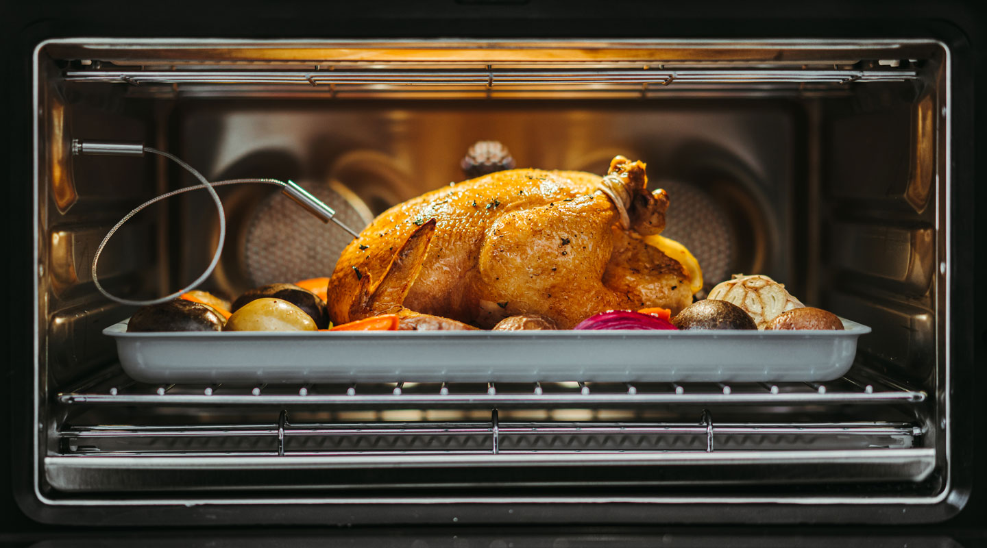 Cooked chicken with potatoes on a June pan connected to the food thermometer inside the June oven